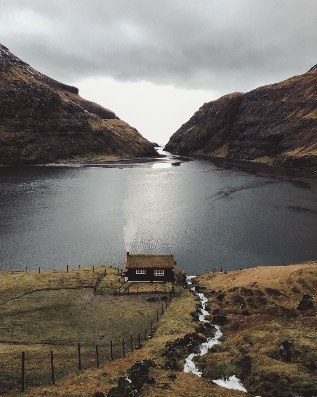 Dark charred wood modern cabin perched over calm deep blue fjord water