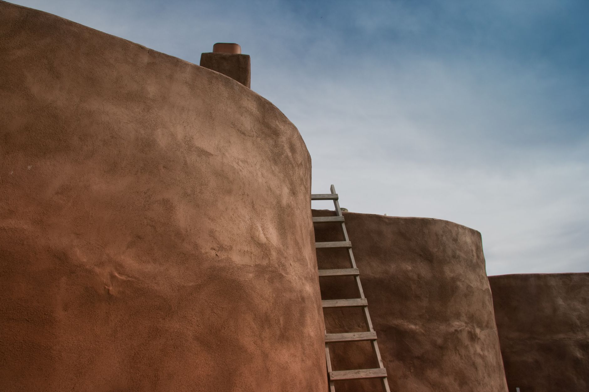Sun-drenched adobe walls with vigas casting geometric shadows across terracotta courtyard